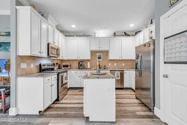 kitchen featuring stainless steel appliances, light wood-style flooring, white cabinetry, a kitchen island, and light stone countertops