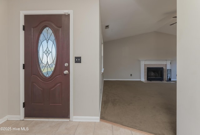 foyer entrance featuring a tiled fireplace, ceiling fan, light colored carpet, and vaulted ceiling