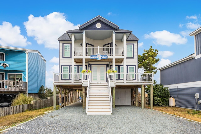 beach home featuring gravel driveway, french doors, a shingled roof, an attached garage, and a carport