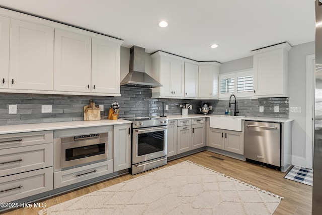 kitchen featuring wall chimney exhaust hood, appliances with stainless steel finishes, a sink, and light countertops