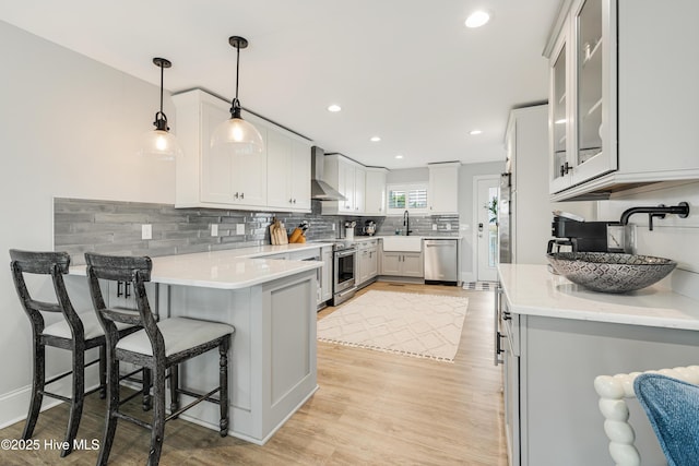 kitchen featuring stainless steel appliances, tasteful backsplash, light countertops, light wood-type flooring, and a peninsula