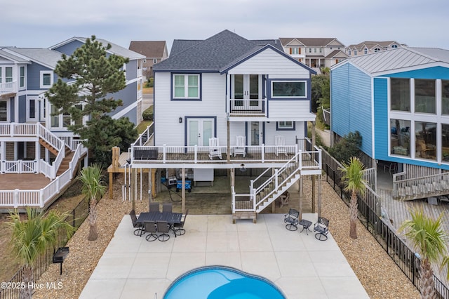 rear view of house with french doors, roof with shingles, stairway, a patio area, and a balcony