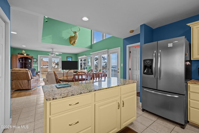 kitchen featuring french doors, light stone counters, cream cabinets, stainless steel fridge with ice dispenser, and a center island