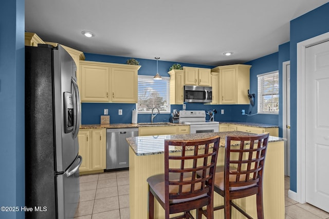 kitchen with hanging light fixtures, light tile patterned floors, a kitchen bar, a kitchen island, and appliances with stainless steel finishes