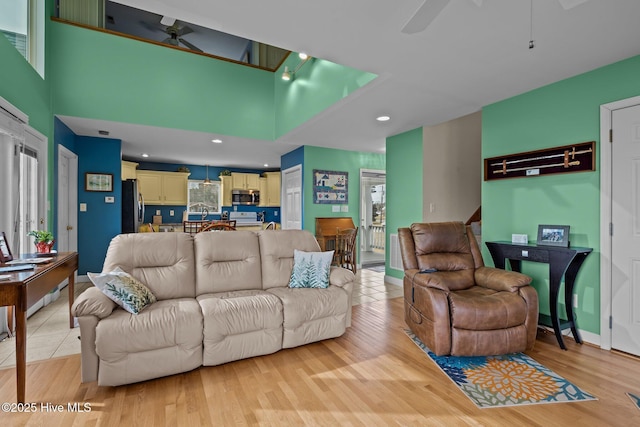 living room featuring ceiling fan, light wood-type flooring, and a towering ceiling