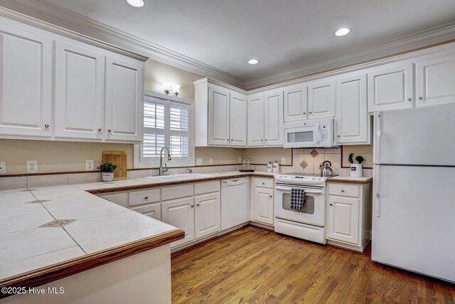 kitchen with sink, kitchen peninsula, white appliances, white cabinets, and light wood-type flooring