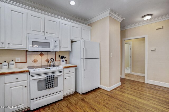 kitchen with kitchen peninsula, a breakfast bar, white appliances, crown molding, and white cabinets