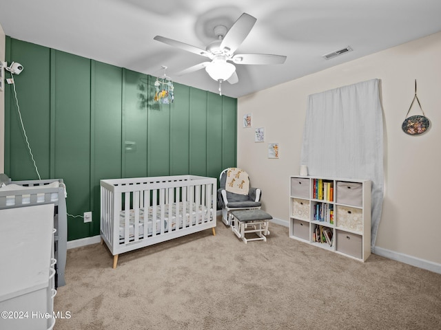 bedroom featuring ceiling fan, light carpet, and a crib