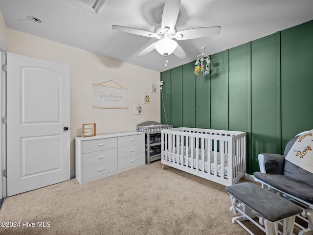 bedroom featuring ceiling fan, light carpet, and a crib