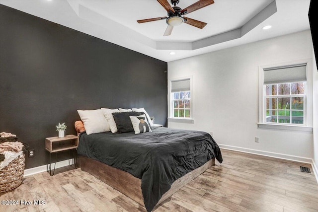 bedroom with light wood-type flooring, a tray ceiling, and ceiling fan