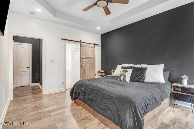 bedroom with a tray ceiling, a barn door, ceiling fan, and light hardwood / wood-style floors