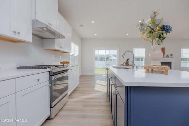 kitchen featuring white cabinets, sink, stainless steel range with gas cooktop, and an island with sink