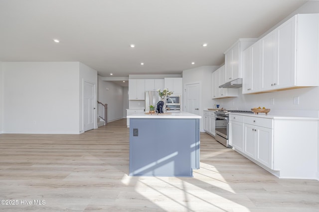 kitchen featuring appliances with stainless steel finishes, light hardwood / wood-style flooring, white cabinetry, and a kitchen island with sink