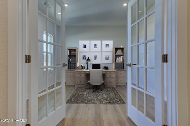 home office with french doors, built in desk, and light hardwood / wood-style flooring