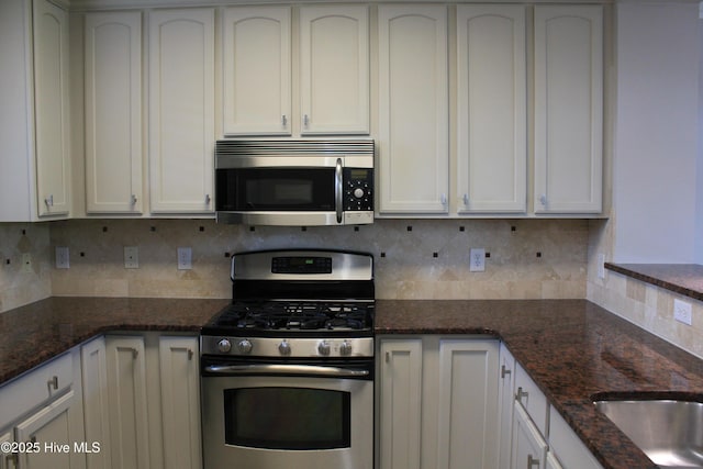 kitchen featuring white cabinets, decorative backsplash, dark stone countertops, and stainless steel appliances