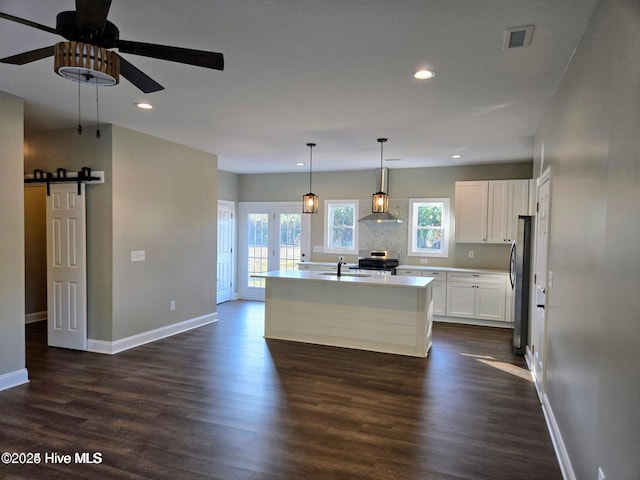 kitchen featuring stainless steel appliances, a barn door, decorative light fixtures, white cabinets, and an island with sink