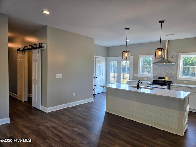 kitchen with white cabinetry, hanging light fixtures, wall chimney range hood, a barn door, and stainless steel range oven