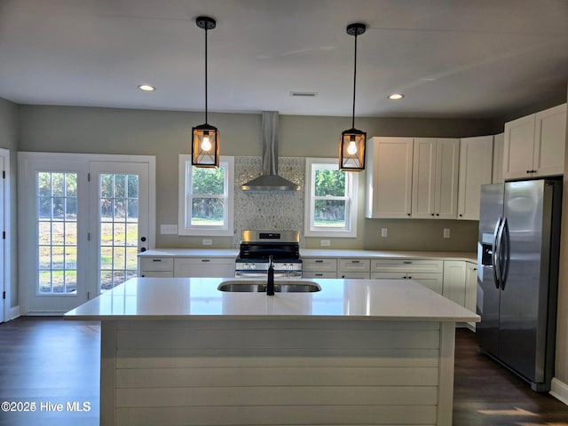 kitchen featuring pendant lighting, an island with sink, stainless steel appliances, and wall chimney range hood