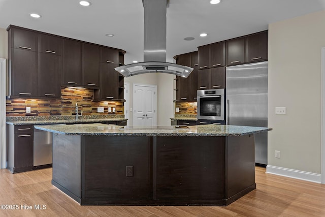 kitchen featuring dark brown cabinetry, stainless steel appliances, stone countertops, island range hood, and a kitchen island