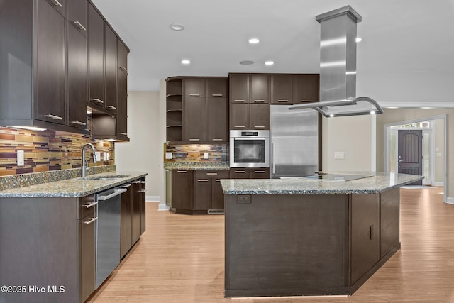 kitchen featuring sink, light stone countertops, appliances with stainless steel finishes, a kitchen island, and dark brown cabinetry