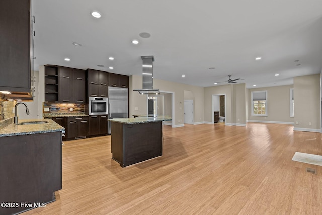 kitchen with appliances with stainless steel finishes, dark brown cabinetry, island range hood, sink, and light hardwood / wood-style floors