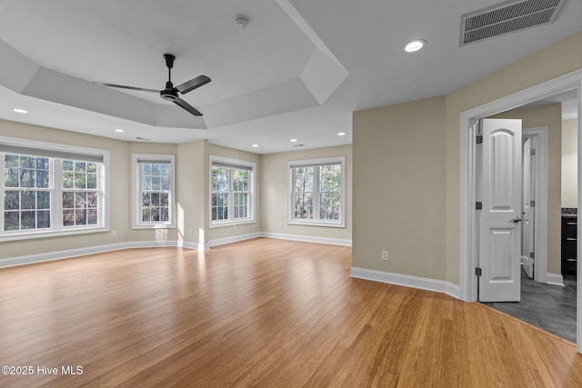 unfurnished living room featuring a tray ceiling, ceiling fan, and light hardwood / wood-style floors