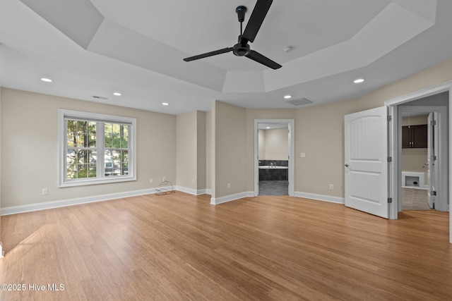 unfurnished living room with ceiling fan, a raised ceiling, and light hardwood / wood-style flooring