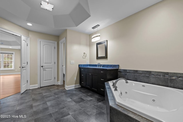 bathroom with a tray ceiling, tiled tub, and vanity