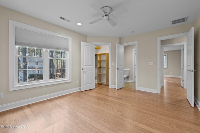 unfurnished bedroom featuring a spacious closet, ceiling fan, ensuite bathroom, a closet, and light wood-type flooring