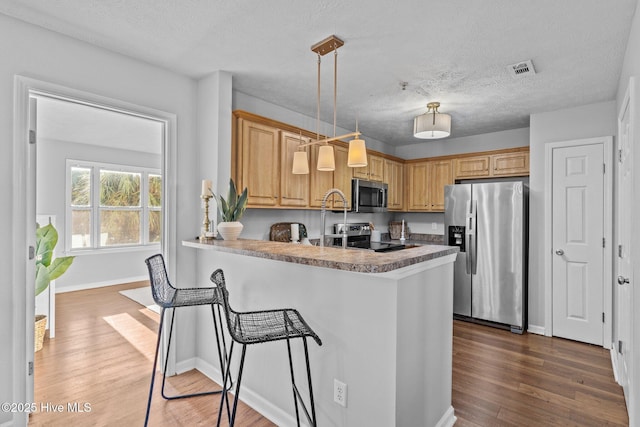 kitchen featuring stainless steel appliances, dark hardwood / wood-style flooring, kitchen peninsula, pendant lighting, and a breakfast bar area