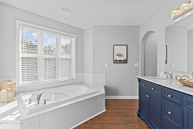 bathroom with hardwood / wood-style floors, vanity, and a relaxing tiled tub