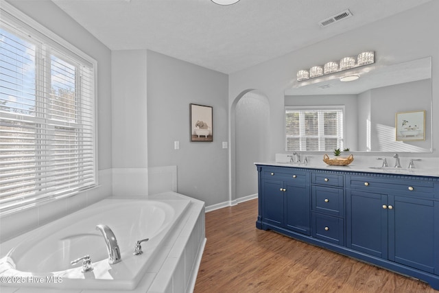 bathroom featuring vanity, wood-type flooring, a textured ceiling, and tiled bath