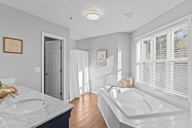 bathroom featuring a textured ceiling, vanity, tiled bath, and hardwood / wood-style flooring