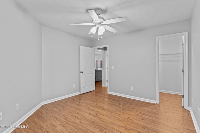 unfurnished bedroom with a walk in closet, ceiling fan, light wood-type flooring, a textured ceiling, and a closet