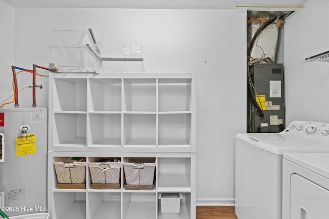 clothes washing area featuring washing machine and dryer, hardwood / wood-style flooring, heating unit, and water heater