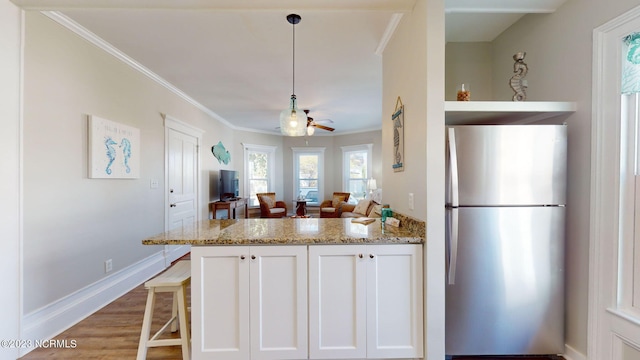 kitchen with white cabinetry, light stone countertops, stainless steel fridge, decorative light fixtures, and a breakfast bar area