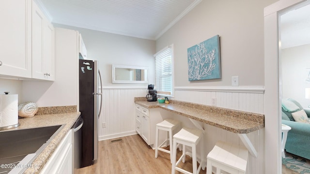 kitchen featuring white cabinets, ornamental molding, appliances with stainless steel finishes, light hardwood / wood-style floors, and light stone counters