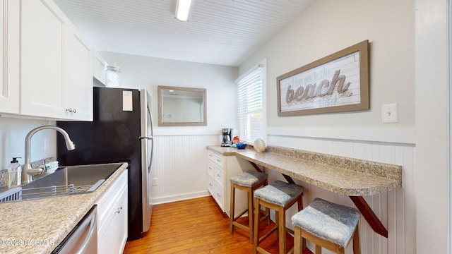 kitchen featuring a kitchen bar, stainless steel dishwasher, sink, white cabinets, and light hardwood / wood-style floors