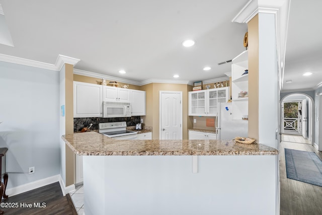 kitchen with white cabinetry, light stone countertops, backsplash, kitchen peninsula, and white appliances