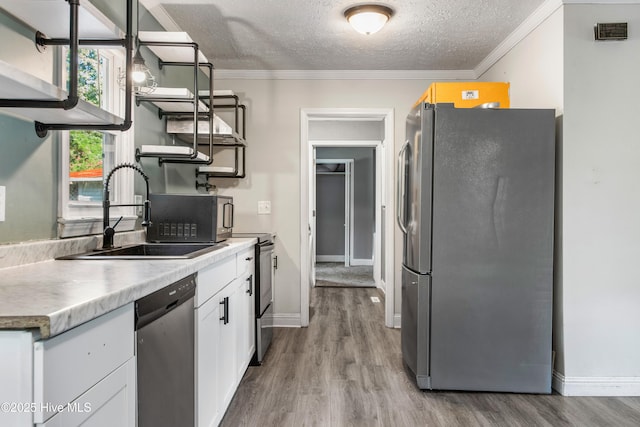 kitchen featuring sink, stainless steel appliances, a textured ceiling, white cabinets, and light wood-type flooring