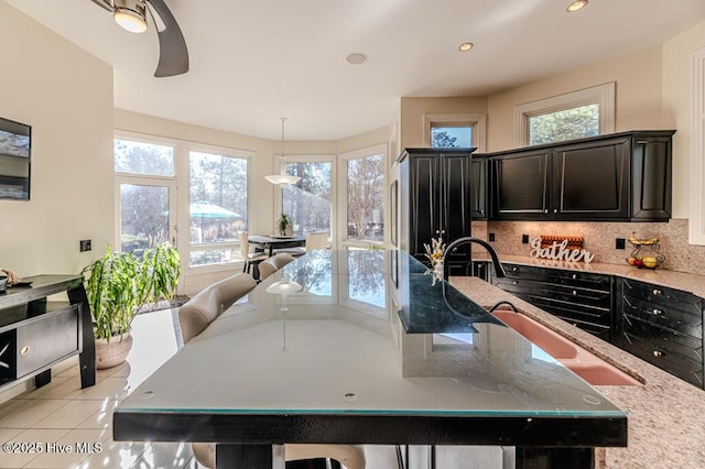 kitchen with tasteful backsplash, light stone counters, a spacious island, sink, and hanging light fixtures