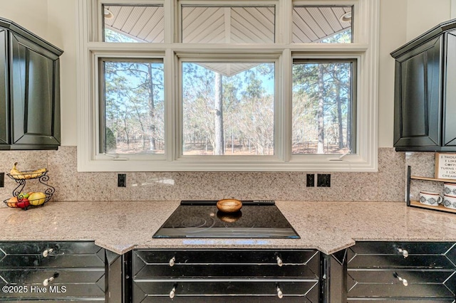 kitchen with oven, light stone counters, black electric cooktop, and decorative backsplash