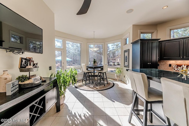 interior space featuring decorative backsplash, a kitchen breakfast bar, ceiling fan, light tile patterned floors, and hanging light fixtures