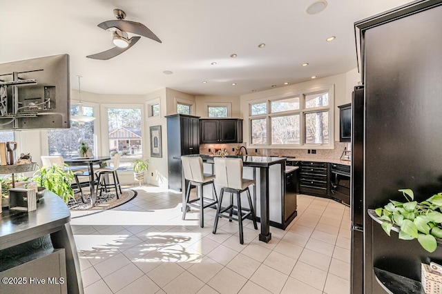 kitchen with decorative backsplash, a breakfast bar, ceiling fan, light tile patterned floors, and a center island with sink