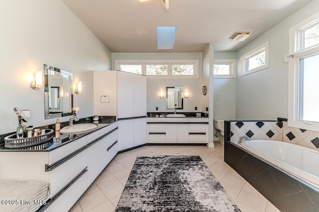 bathroom with tile patterned floors, a relaxing tiled tub, vanity, and a skylight