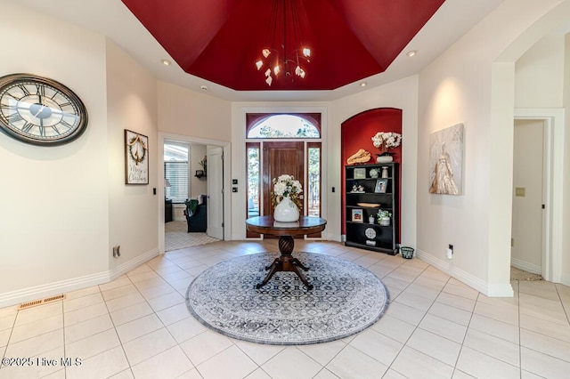 foyer entrance featuring light tile patterned floors, a raised ceiling, and a high ceiling