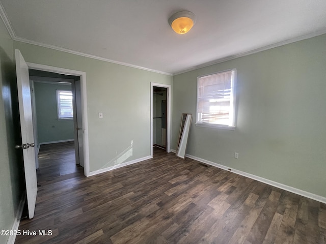 unfurnished bedroom with a walk in closet, a closet, dark wood-type flooring, and ornamental molding