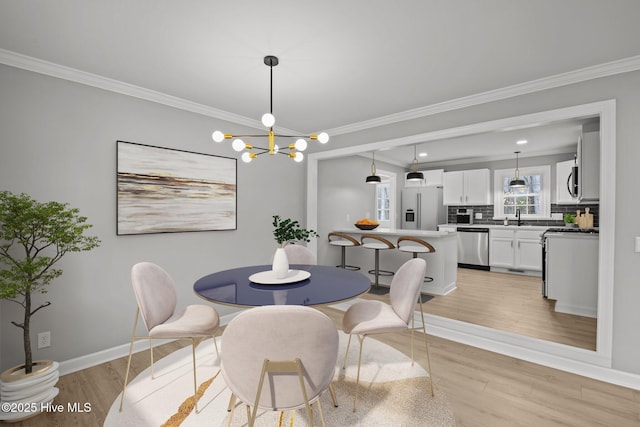 dining area with sink, a chandelier, crown molding, and light hardwood / wood-style floors