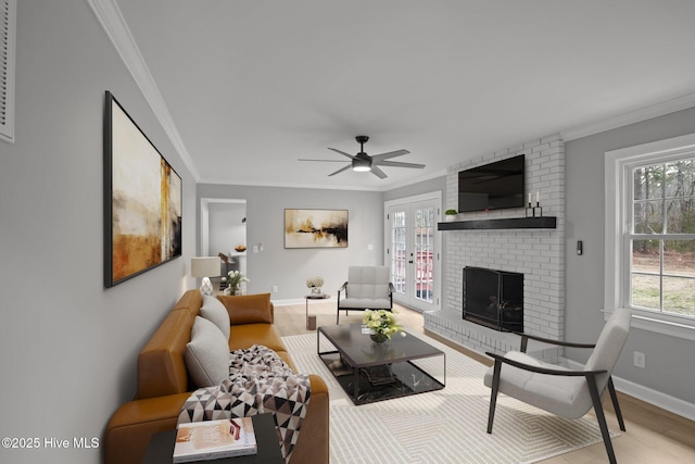 living room with light wood-type flooring, ceiling fan, a brick fireplace, and crown molding