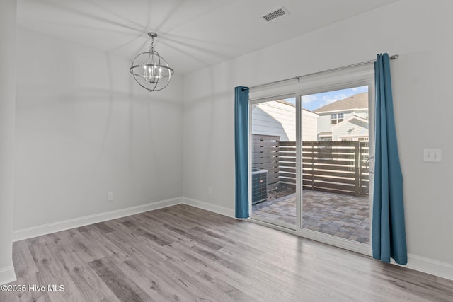 spare room featuring a chandelier and light hardwood / wood-style floors